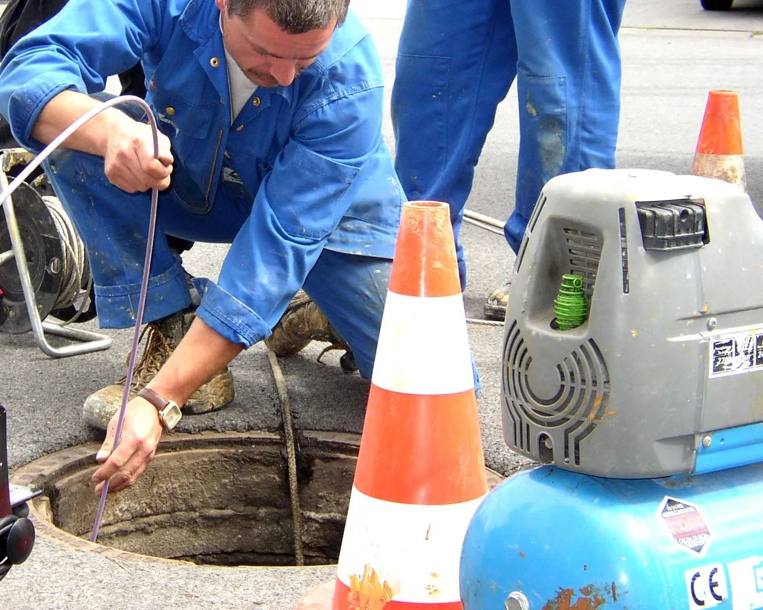 Technician running a sewer camera line into a street-level access point