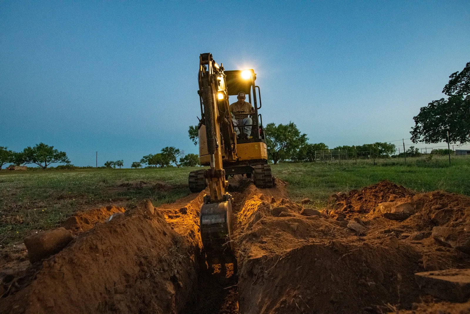 Excavator digging an open trench for a sewer line replacement